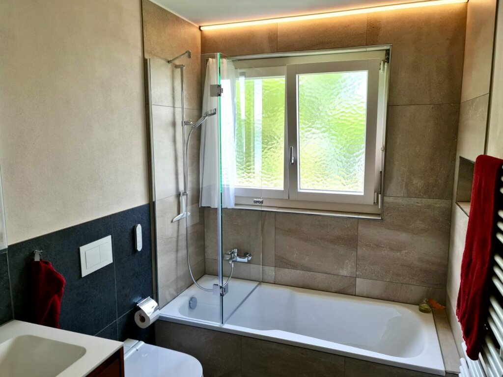 Saniertes Bad mit Badewanne, Glasabtrennung und grossformatigen Platten