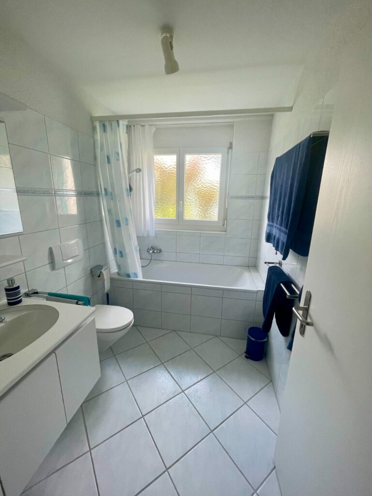 Altes Bad mit weissen Fliesen und Duschvorhang an der Badewanne