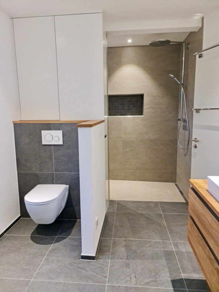 Saniertes Bad mit Wand-WC, Einbauschrank über dem WC und bodenebener Walk-in-Dusche mit Nische